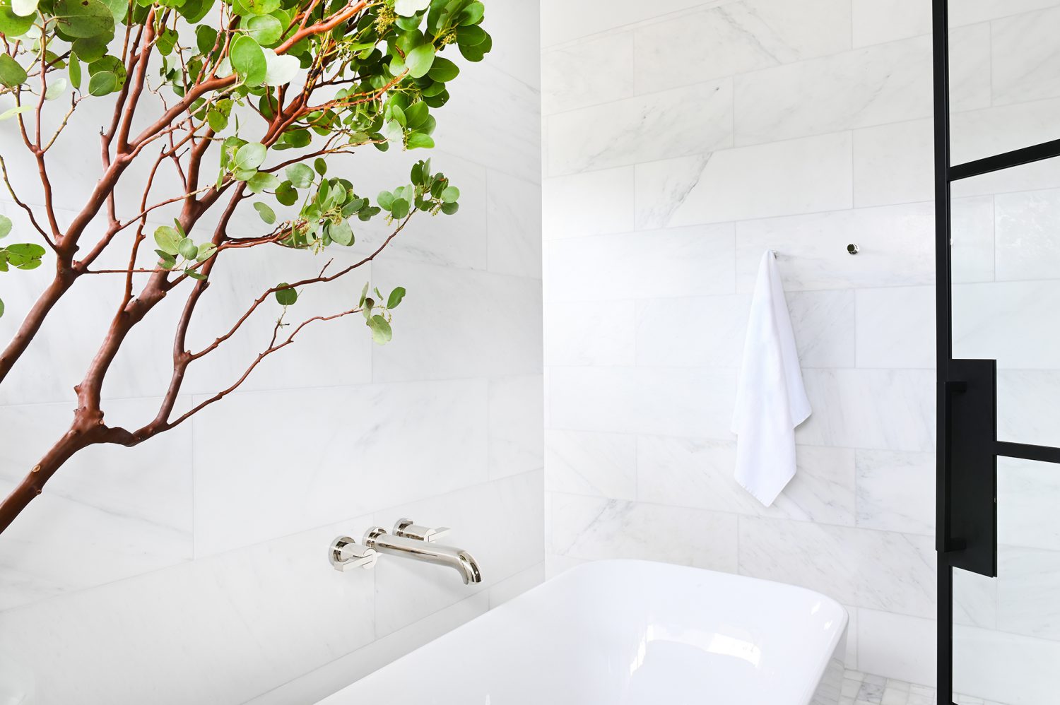 Ferme Moderne bath tub with marble backsplash and green tree designed by Midland Premium Properties in Vancouver, BC